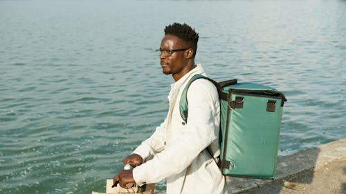 Man with Sunglasses Carrying a Backpack near the Sea