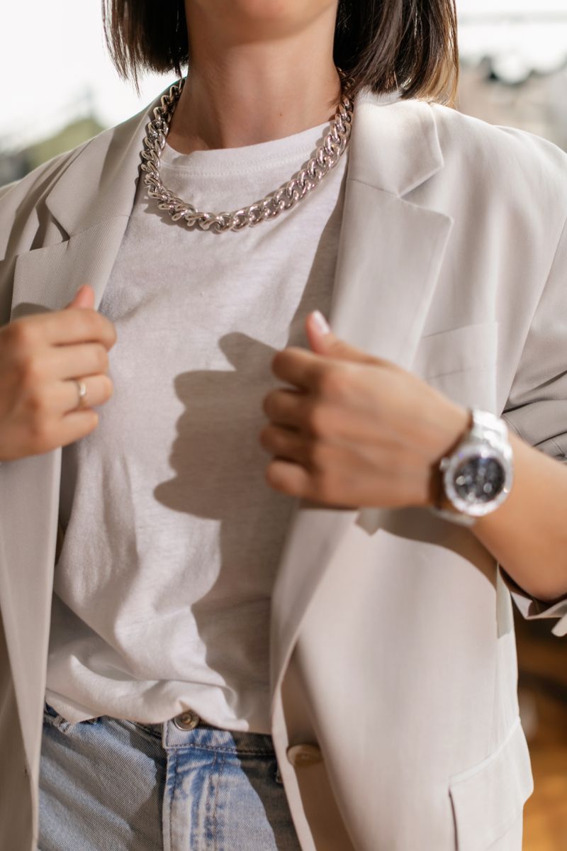 Close-up of a grey blazer, white tee, jeans and a chunky silver-tone necklace