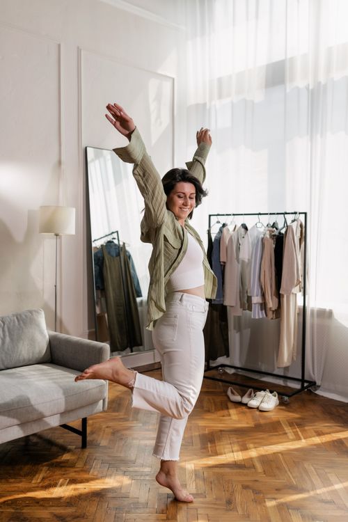 Free Woman expressing joy while balancing on one leg in a stylish room setting. Stock Photo