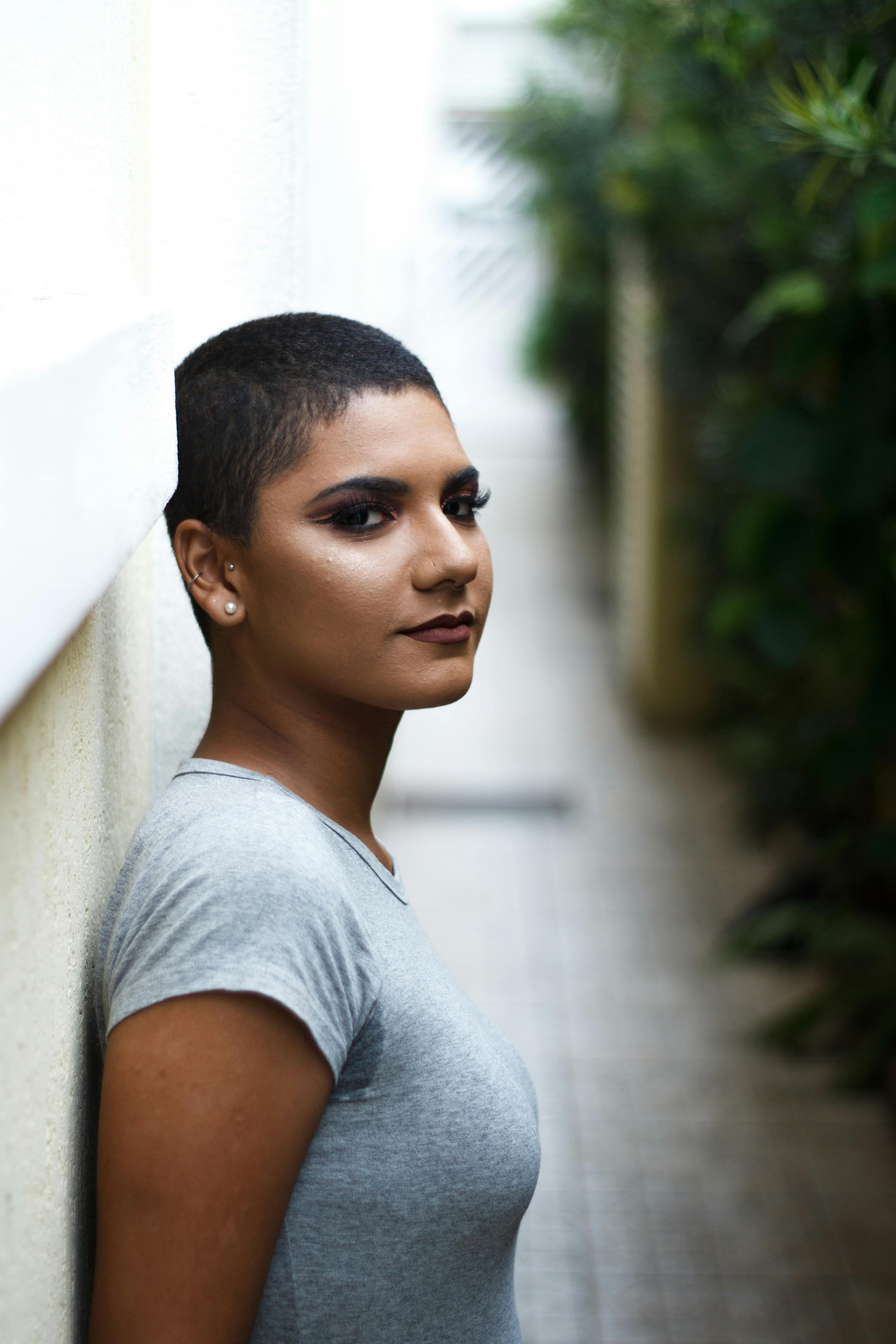 一位留着平头、神情泰然自若的女人靠在户外墙上，显得十分自信