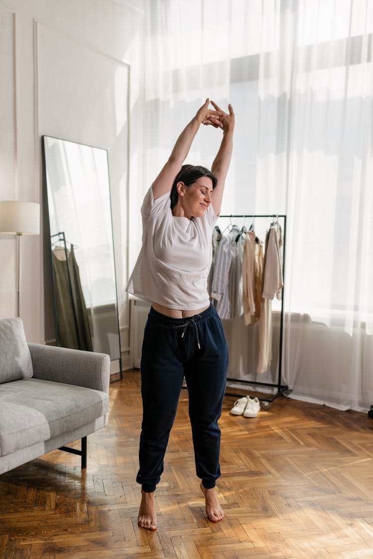 Full Shot Of A Woman In White Shirt And Sweatpants Stretching 