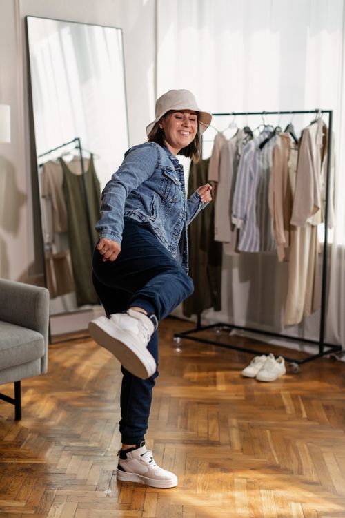 Free Smiling woman in casual wear kicking playfully in a stylish indoor setting. Stock Photo