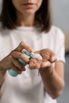 Close-up of a woman applying skin care cream from a dispenser onto her hand indoors.