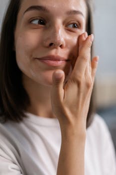 Young woman applying facial cream as part of her skincare routine, showcasing healthy and glowing skin.