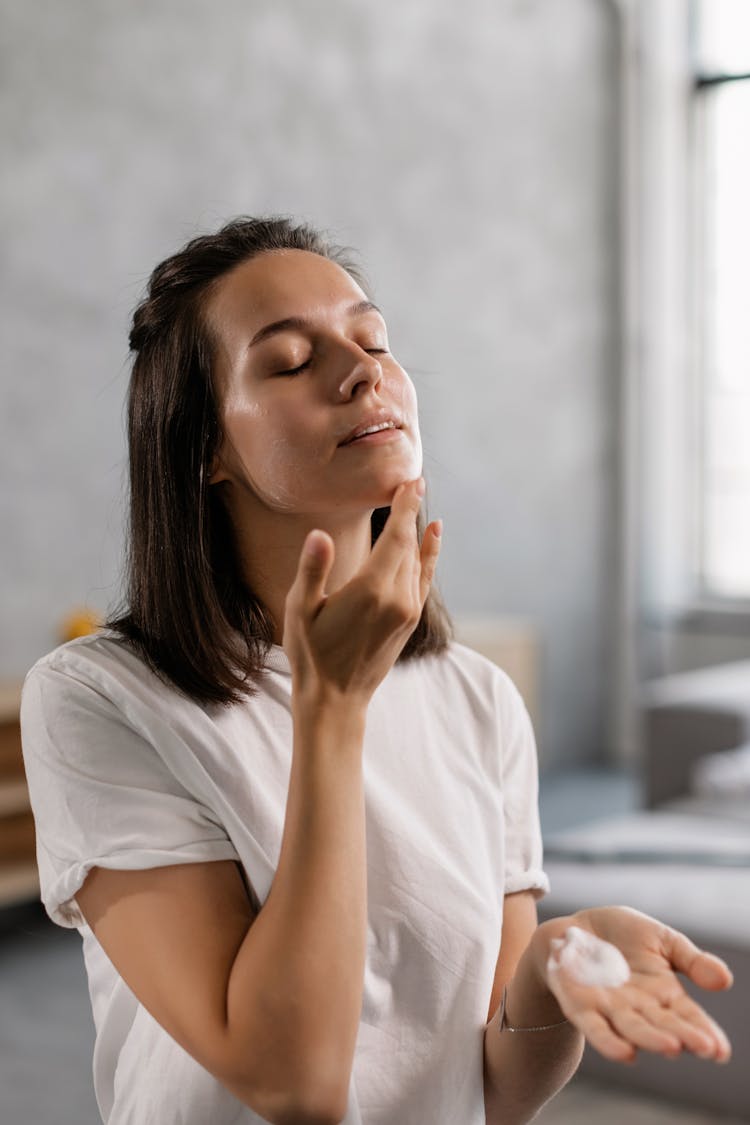 A Woman In White T-shirt Applying Cream On Chin