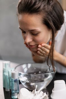 Young woman washing her face with skincare products in a serene home setting.