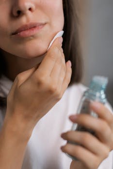 Close-up of a woman applying skincare product to her face with a cotton pad, showcasing beauty care routine.