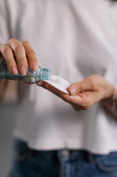Close-up of hands pouring skincare product onto a cotton pad for cosmetic application.