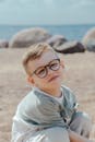 一个戴着眼镜的开朗小男孩坐在晴朗的蓝天下的沙滩上