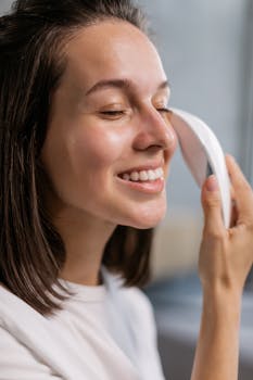 A woman enjoys a facial care routine using a modern massage tool, smiling in a close-up shot.
