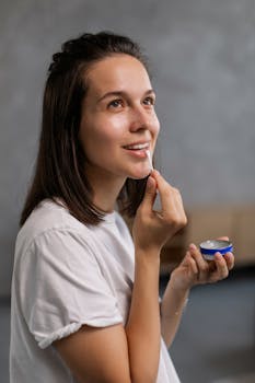 Woman in a white shirt applies lip balm with a smile, showcasing a skincare routine.