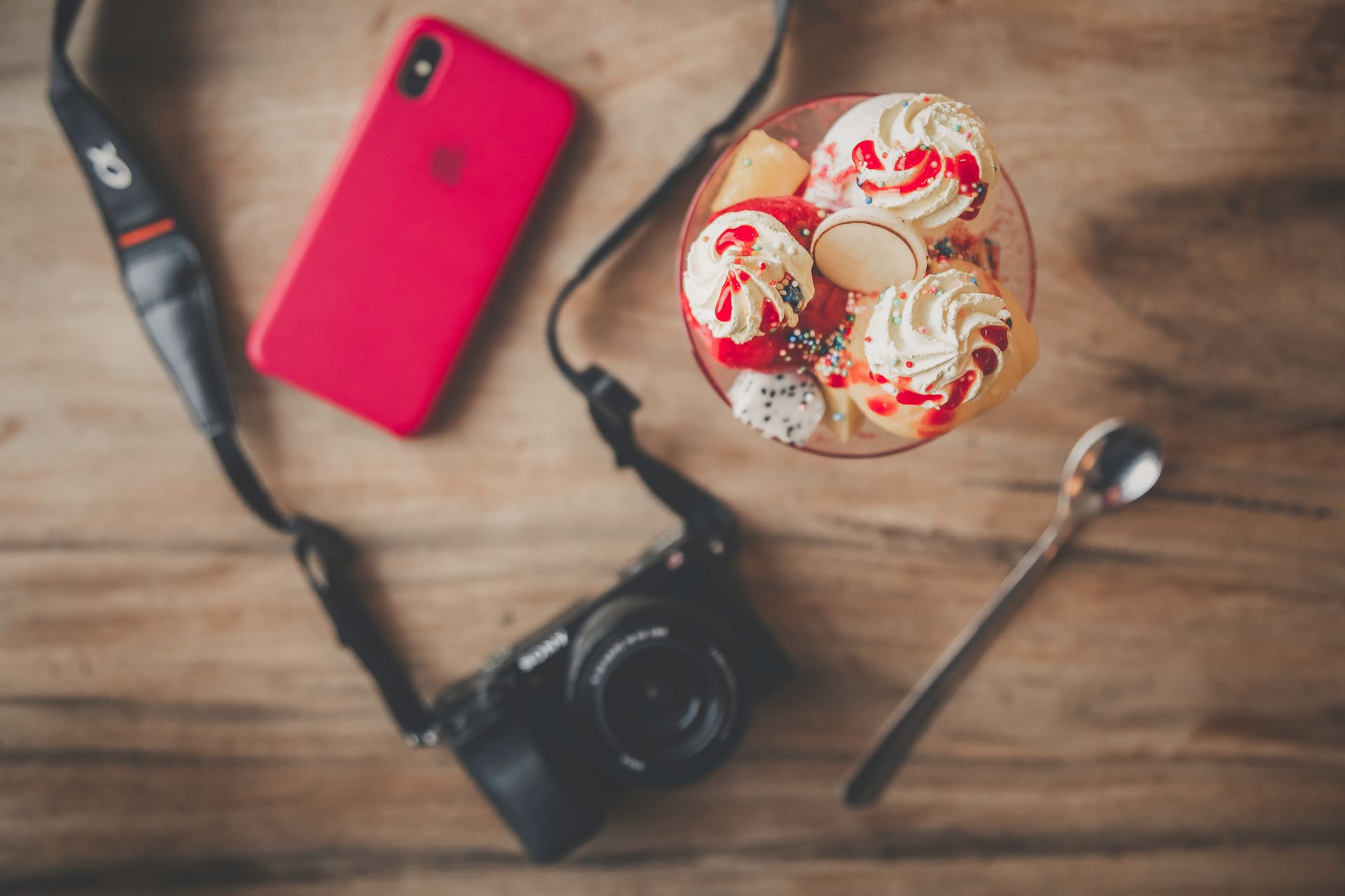 Top view of a vibrant dessert with a camera and smartphone on a wooden table.