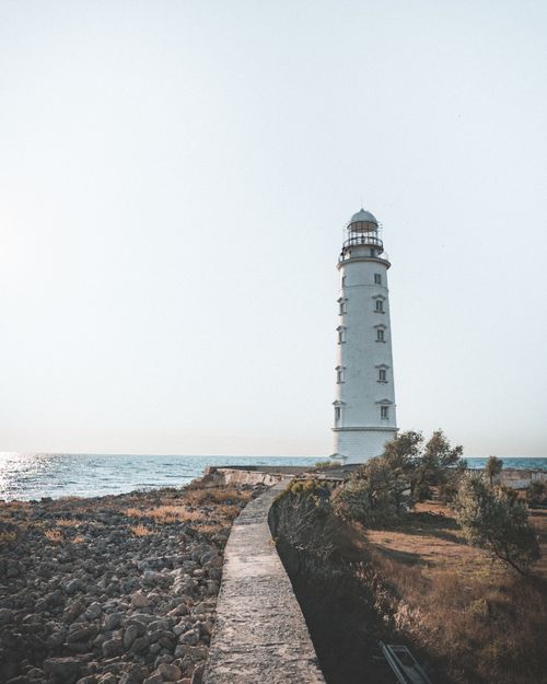 Free A scenic view of the Sevastopol lighthouse by the rocky shore under a clear sky. Stock Photo