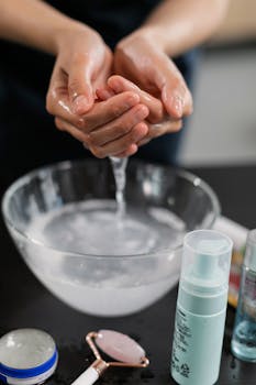 Close-up of a person washing hands, surrounded by skincare products including cosmetics and tools.