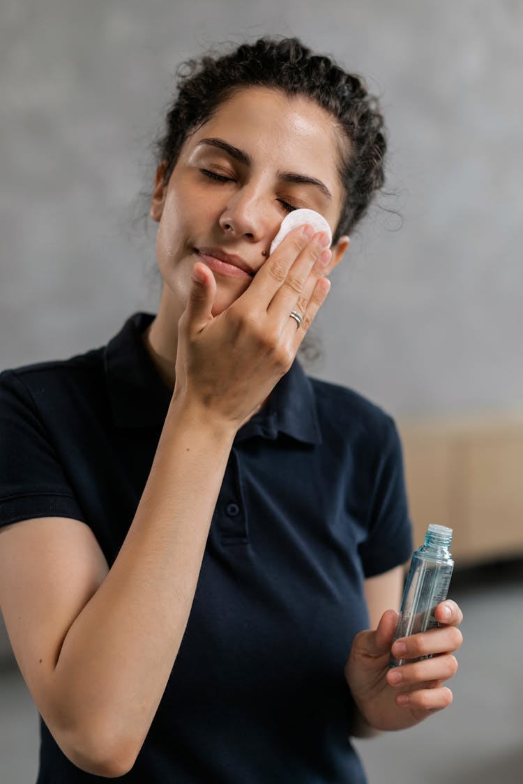 Woman In Black Polo Shirt Holding A Cotton Pad On Her Face 