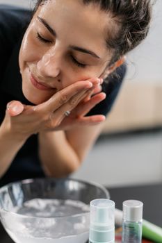 Close-up of a woman washing her face with skincare products in an indoor setting.