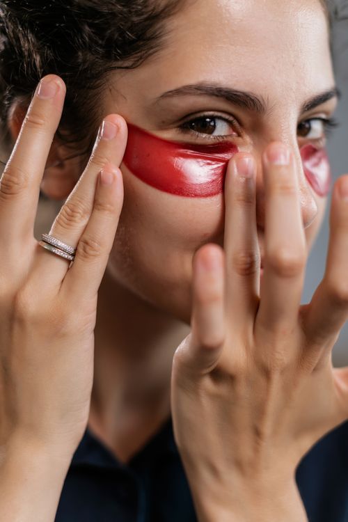 Free Young woman applying red under eye masks for skincare in a close-up shot. Stock Photo
