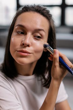 Woman using a makeup brush for facial application inside a well-lit room.