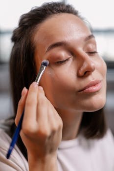 Close-up of a woman applying eye shadow with a makeup brush, focusing on beauty and cosmetics.