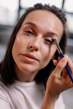A woman applying eye shadow with a brush in a close-up indoor setting.