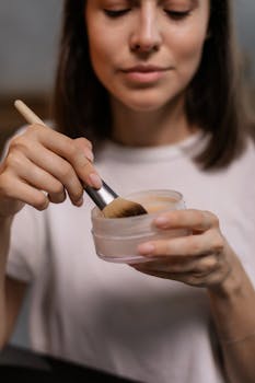 A woman gently applies makeup using a brush, showcasing beauty routine essentials.