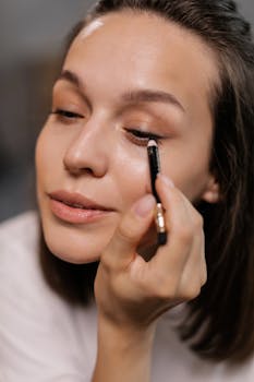 A woman applying eyeliner with precision, showcasing a makeup routine in a close-up shot.