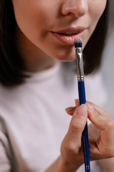 Woman applying makeup on lips using a brush in a close-up shot indoors.