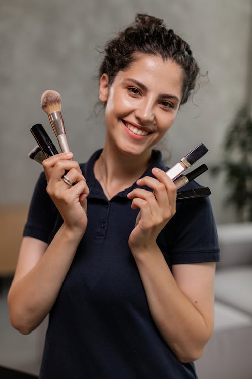 Woman in Black Polo Shirt Holding Makeups and Brushes 