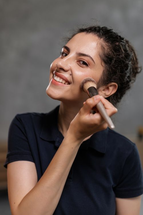 Free Portrait of a smiling woman applying makeup using a brush indoors. Stock Photo