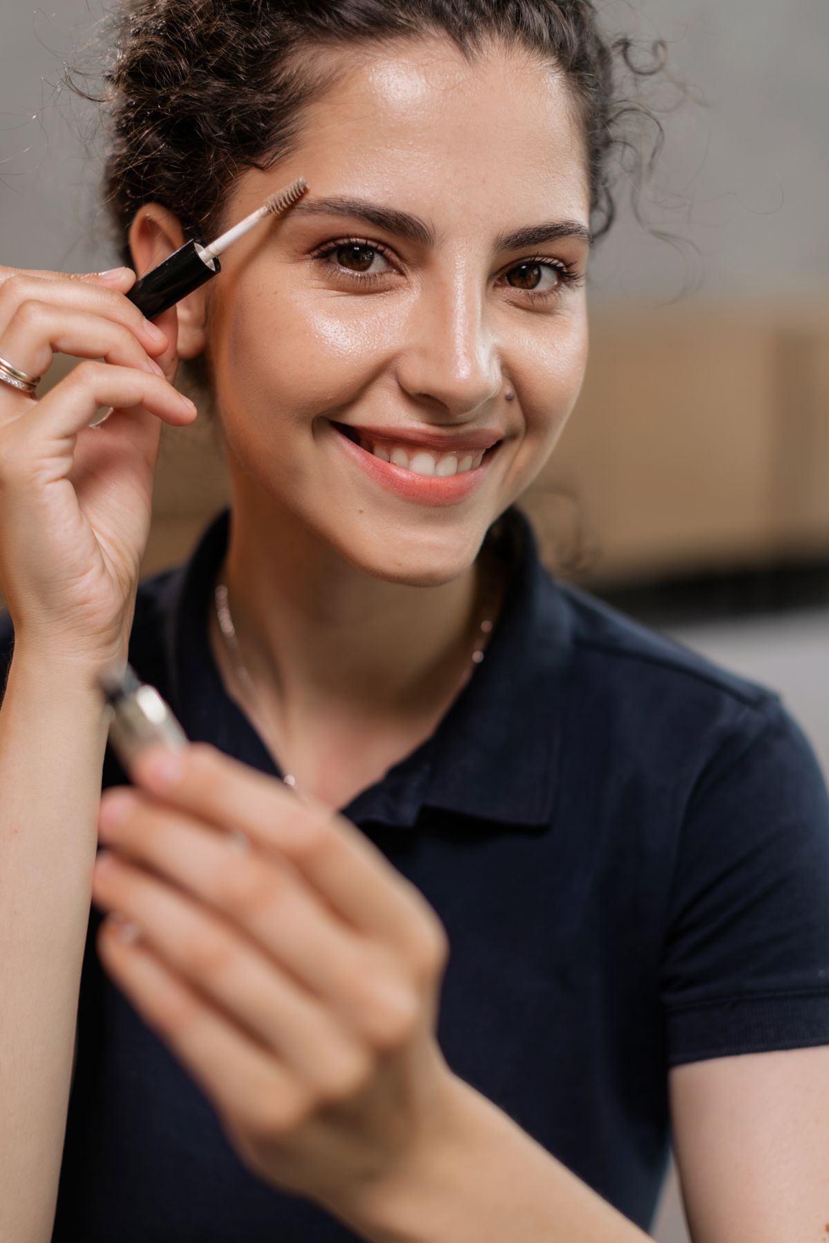 Young woman with curly hair applying eyebrow makeup with a fine pencil