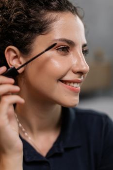 A cheerful woman applies mascara, highlighting her makeup routine and joyful expression.