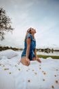 Woman in Blue Sleeveless Dress Sitting on White Textile Near Body of Water