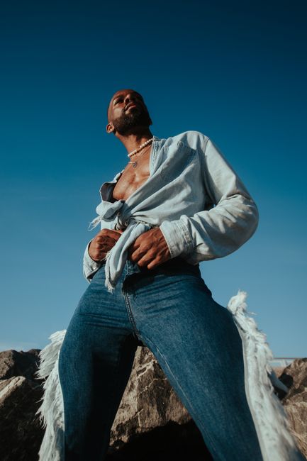 Confident man posing in denim against a blue sky, showcasing stylish fashion.