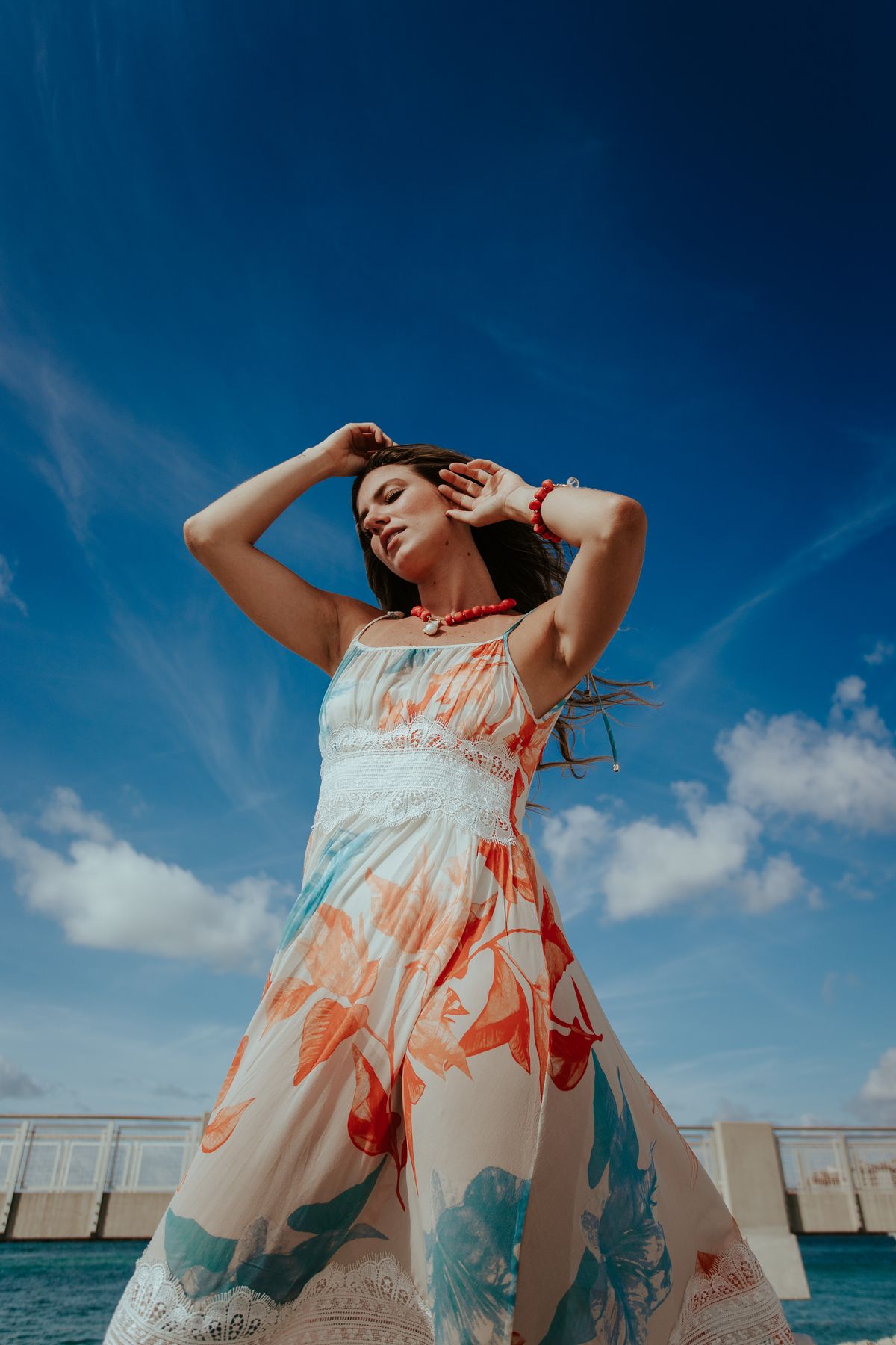 A woman in a white and red floral dress raising her hands joyfully