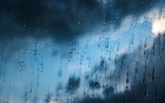 Close-up of raindrops on glass against a dark stormy sky, creating a moody atmosphere.