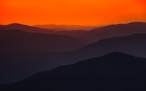 Free Stunning view of a sunset casting orange hues over layered mountain silhouettes. Stock Photo