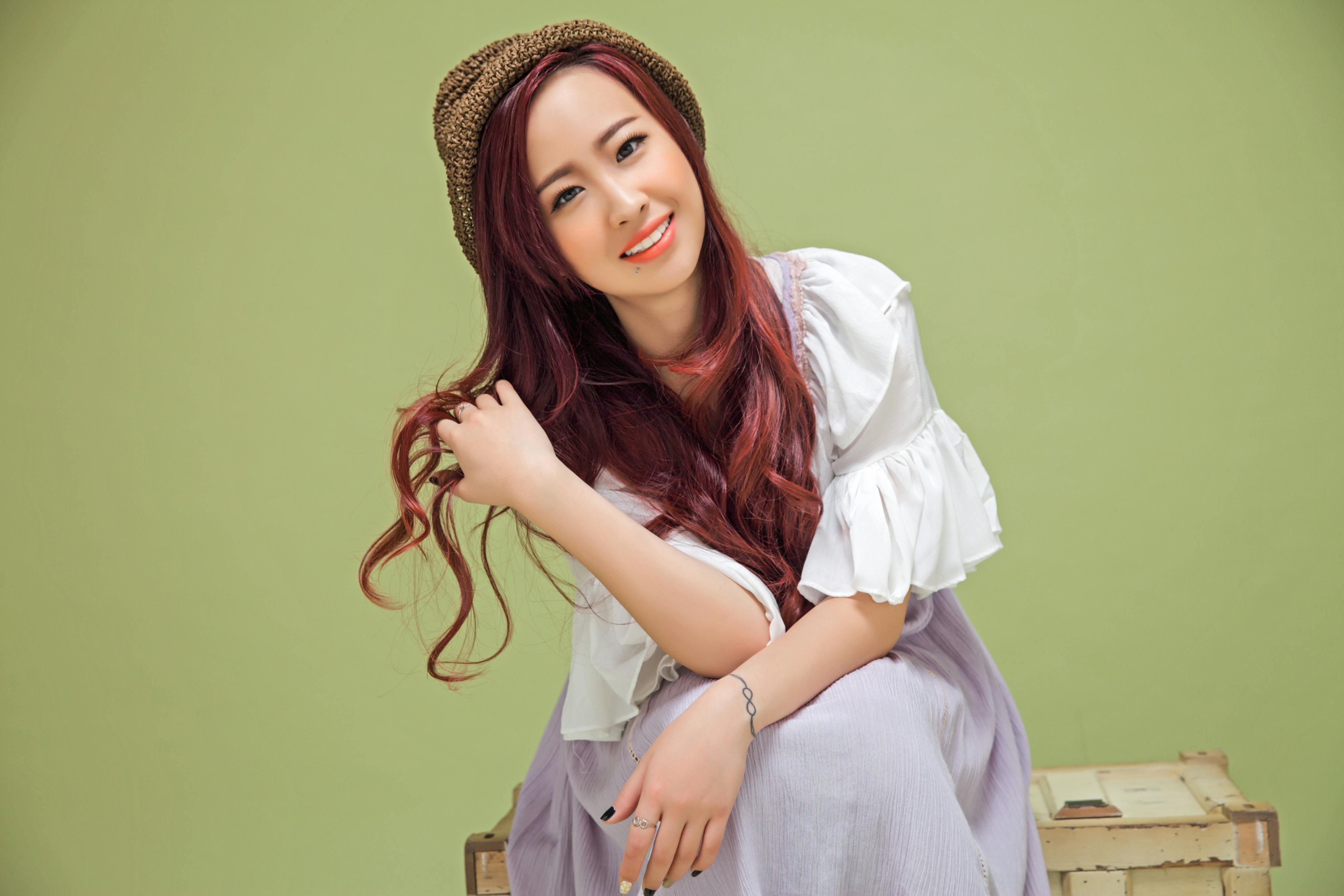Charming woman in a hat and dress poses against a green backdrop with a warm smile.