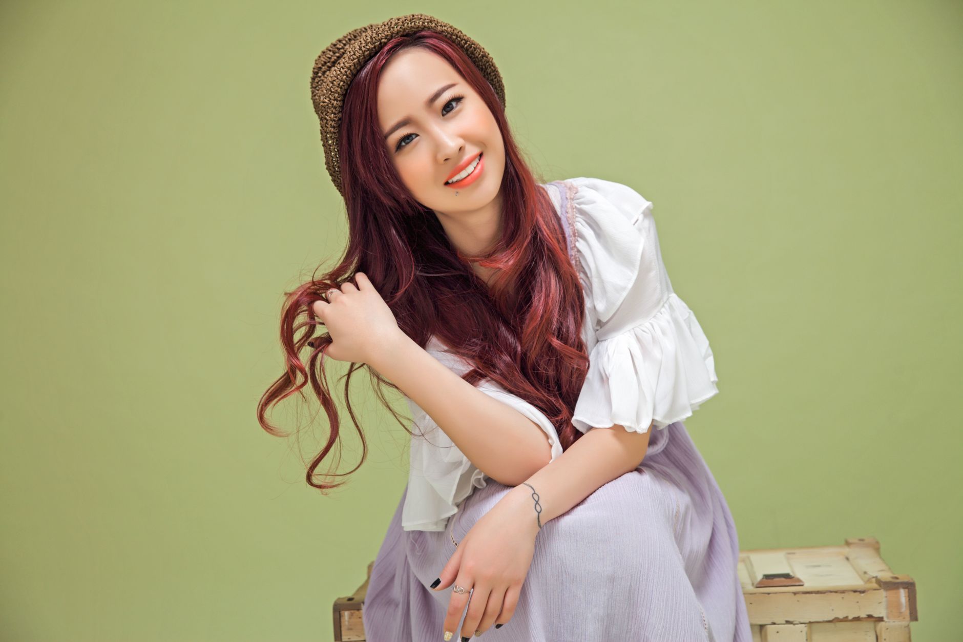 Charming woman in a hat and dress poses against a green backdrop with a warm smile.
