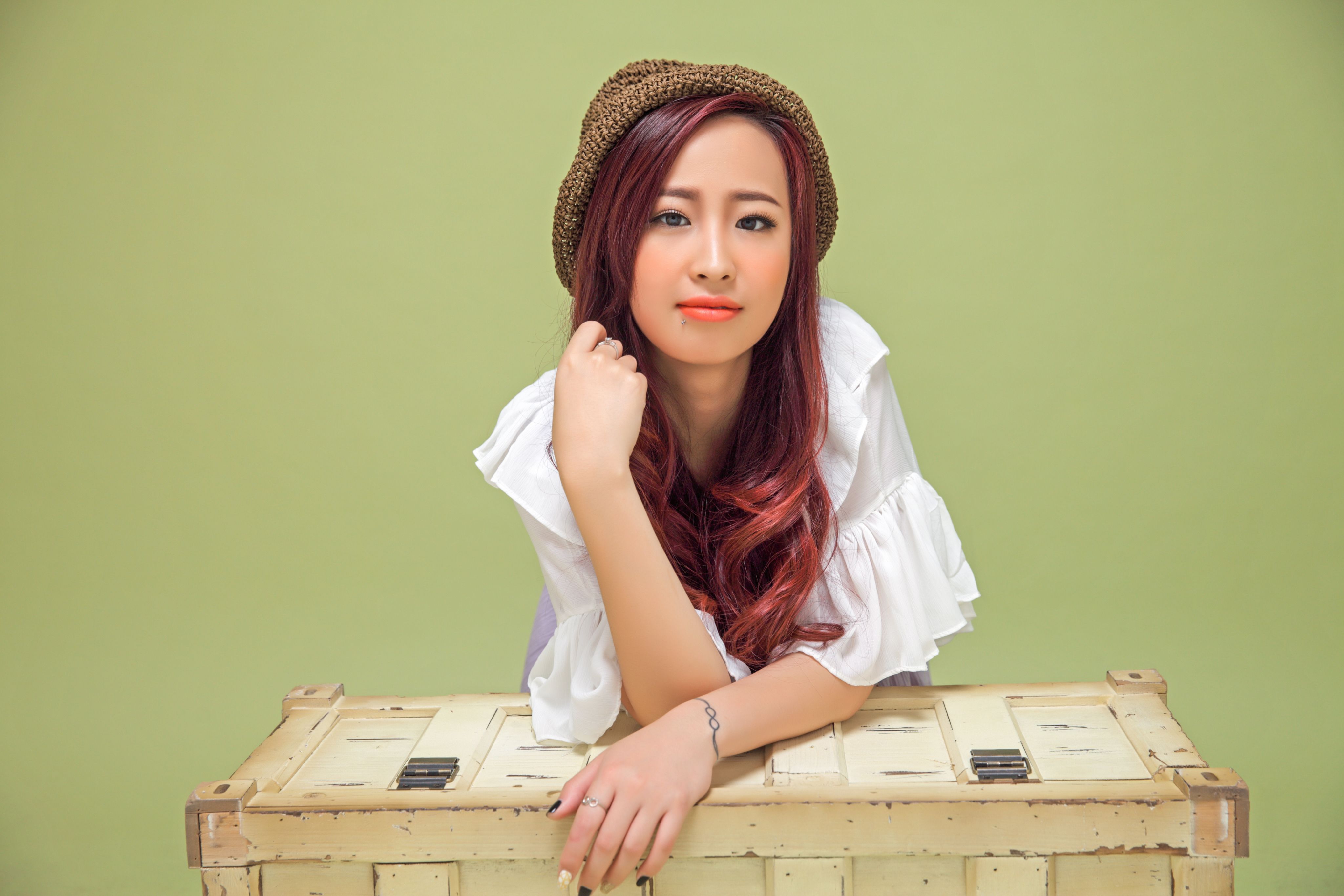 Portrait of a stylish woman leaning on a wooden box with a green background.