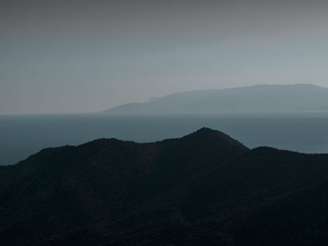 Moody silhouette of a mountain under a foggy sky with a distant sea view.