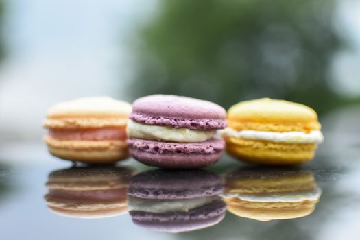 Three colorful macarons with reflections on a glossy surface, showcasing vibrant hues.