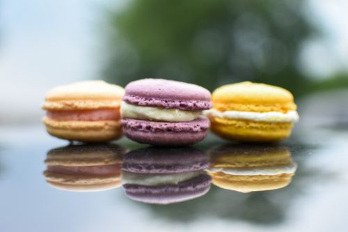 Free Vibrant macarons with cream filling against blurred greenery, showcasing reflections on a shiny surface. Stock Photo
