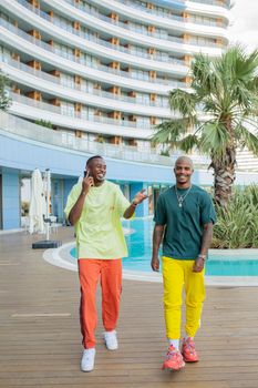 Two men in bright attire enjoying a sunny day by the poolside, laughing and talking.