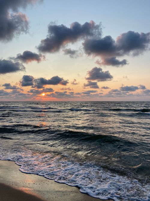 Free Beautiful sunset over the ocean with waves crashing on the sandy shore. Stock Photo