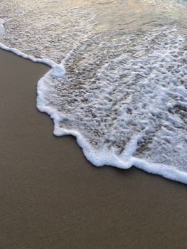 Gentle waves and white foam meet the sandy shore at sunset, capturing a tranquil beach moment.