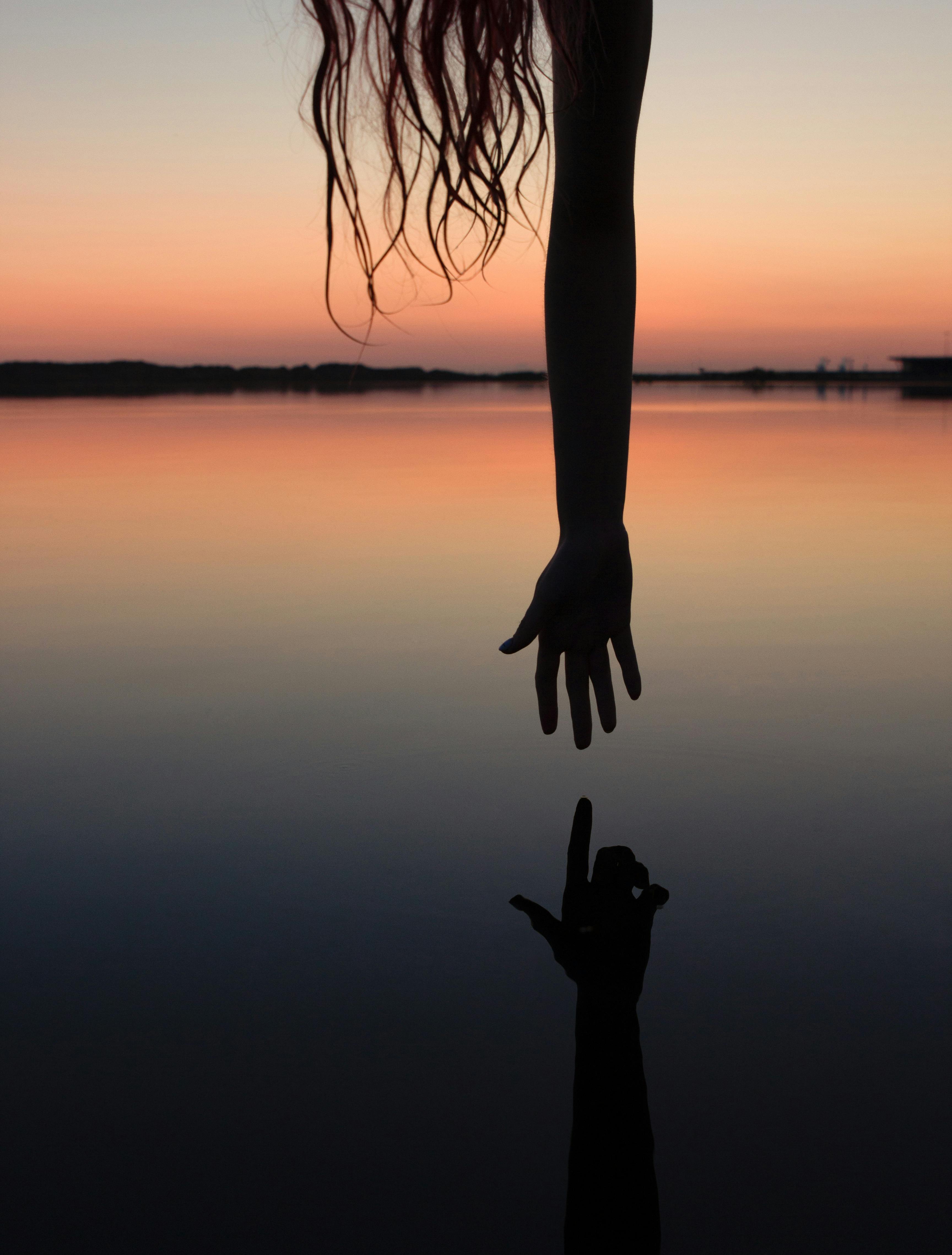 silhouette of person hand reaching water surface