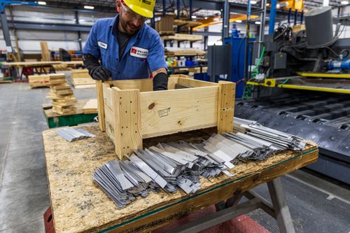 Free Man in safety gear sorting metal pieces at a factory with wooden crates. Stock Photo