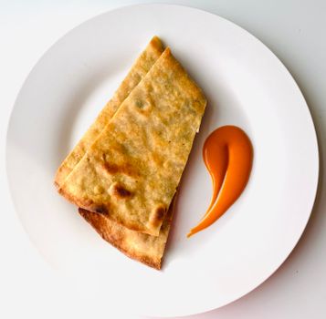 Top view of toasted flatbread served with a tangy orange sauce on a white plate.