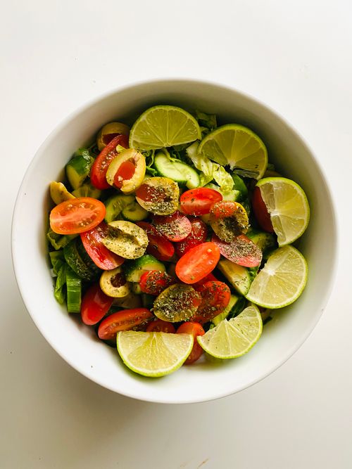 Free Colorful salad with lime, cherry tomatoes, and olives in a white bowl. Stock Photo