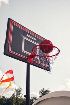 Close-up of a basketball hoop with a red rim outdoors, under a clear sky.